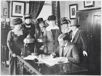 Le gouverneur Carl Elias Milliken signant le projet de loi sur le suffrage sous le regard de six femmes, 1917